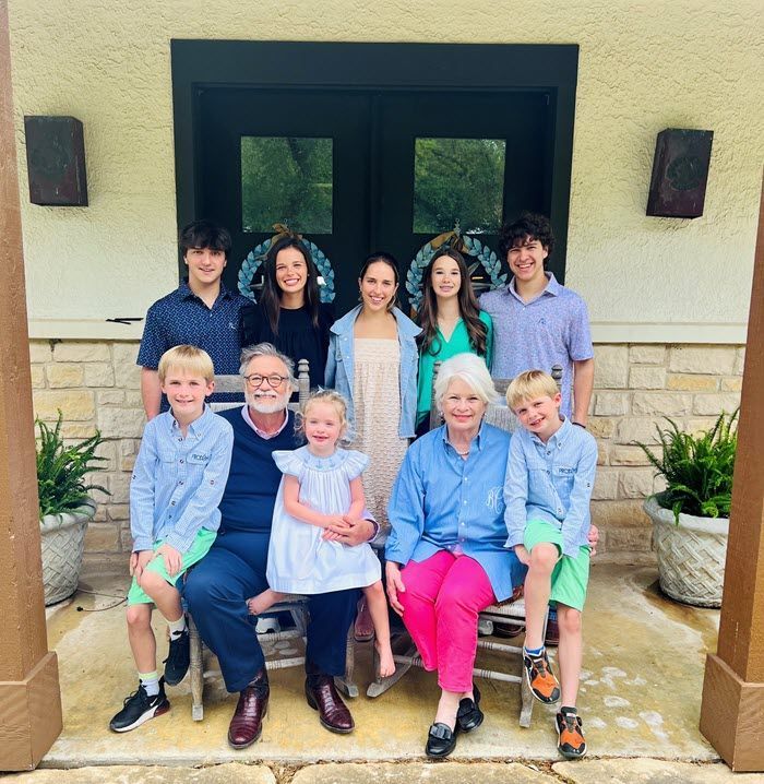 Family posing together on a porch in front of a dark double door, with some seated and others standing.