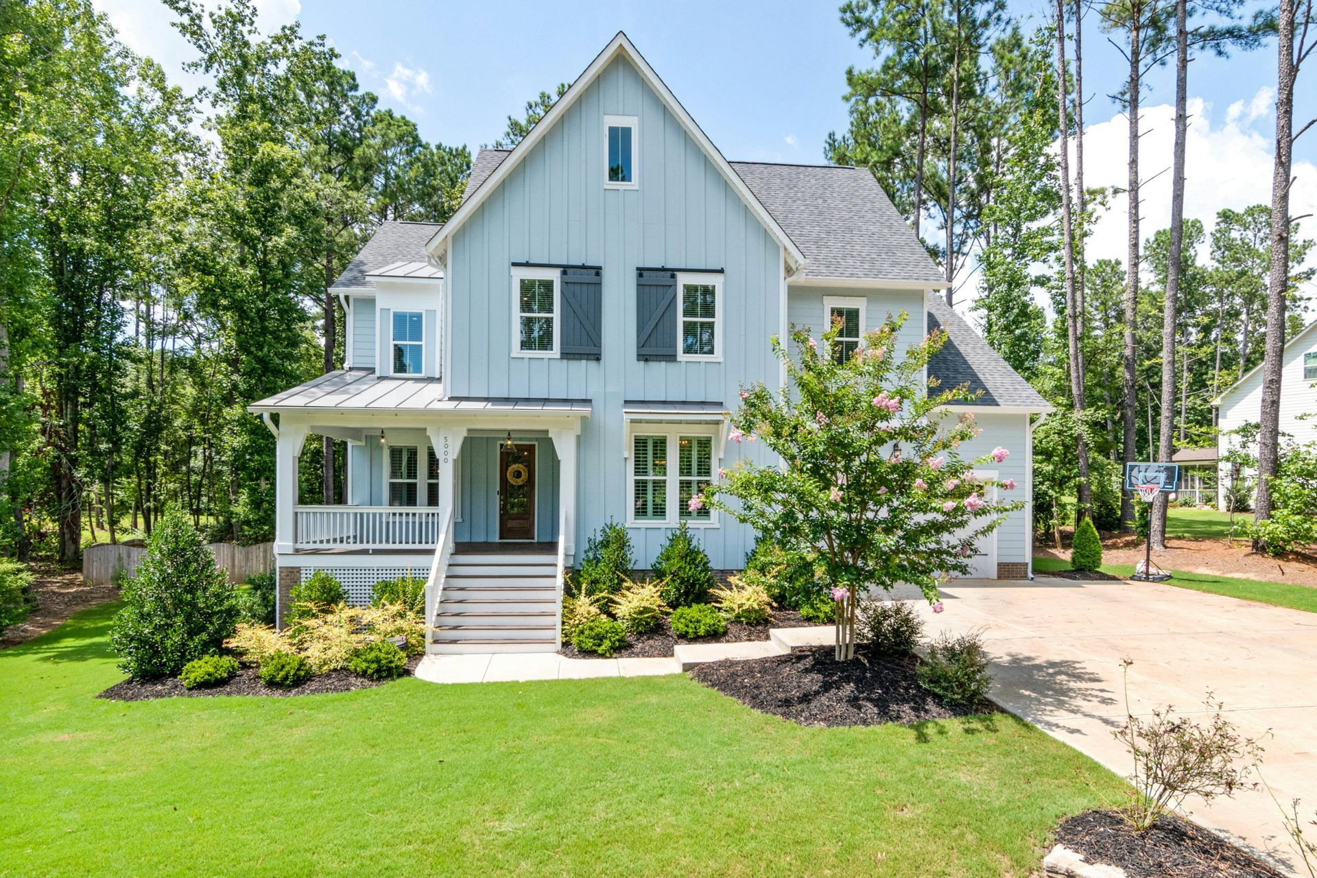 Light blue two-story house with a porch and dark shutters, surrounded by trees and green grass.