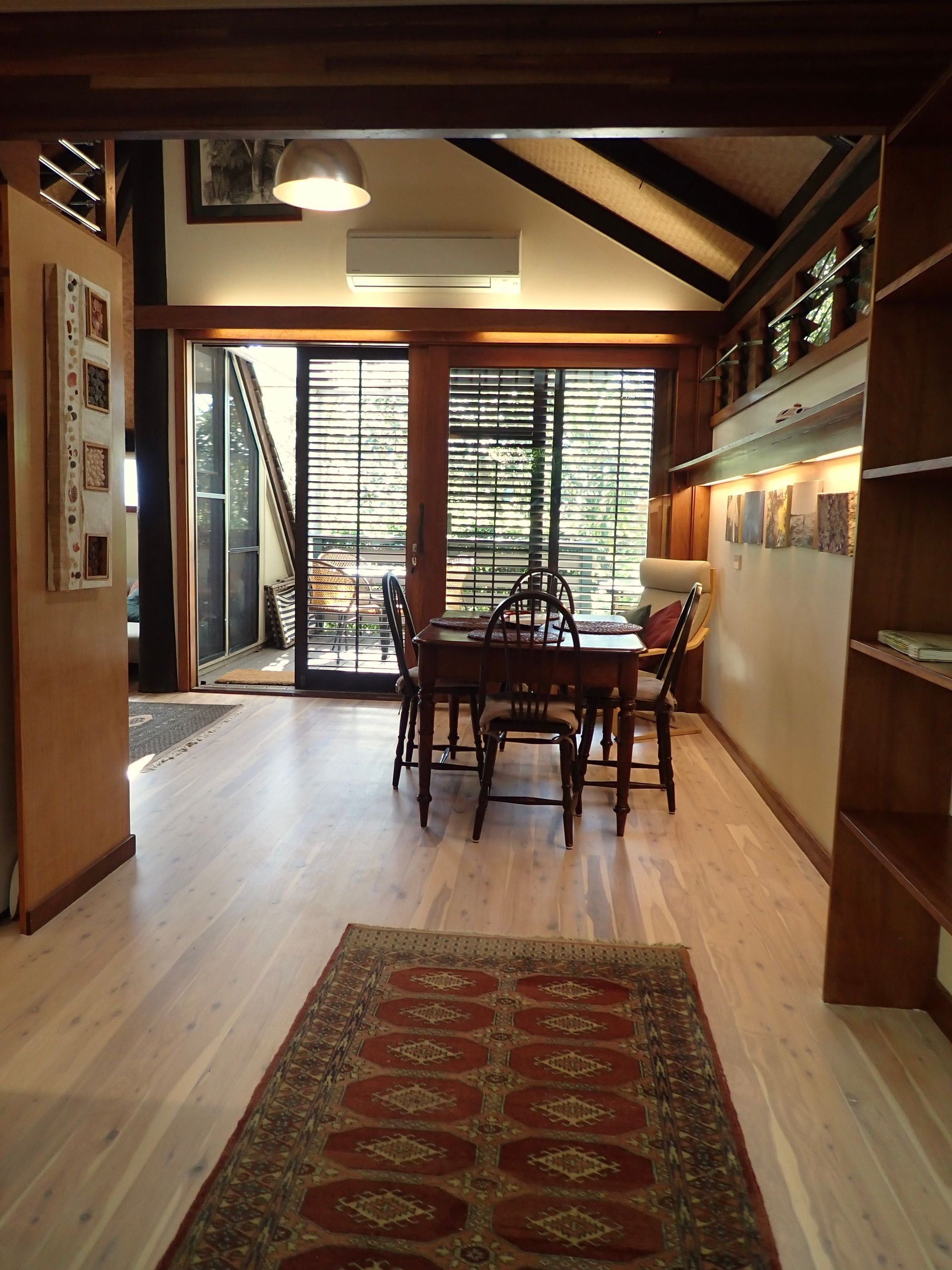 Long dining room with wooden beams, table, chairs, and open doors to a balcony.