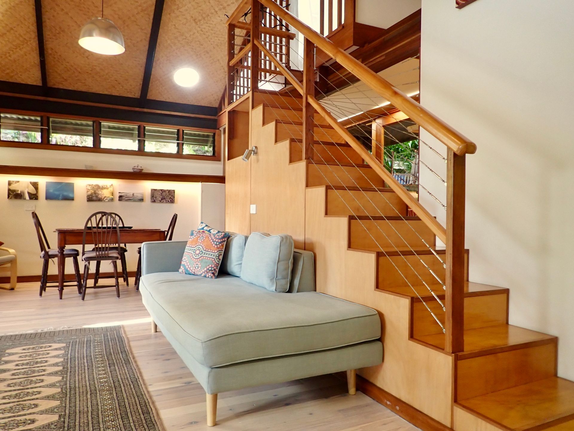 Modern living room with a wooden staircase, light blue sofa, and dining area in the background