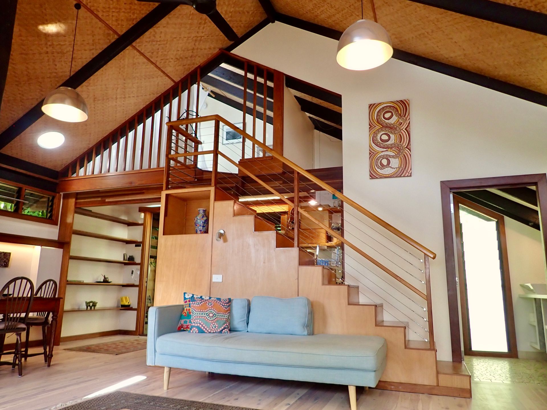 Loft-style living room with blue sofa, wood staircase, high ceiling, and hanging lights