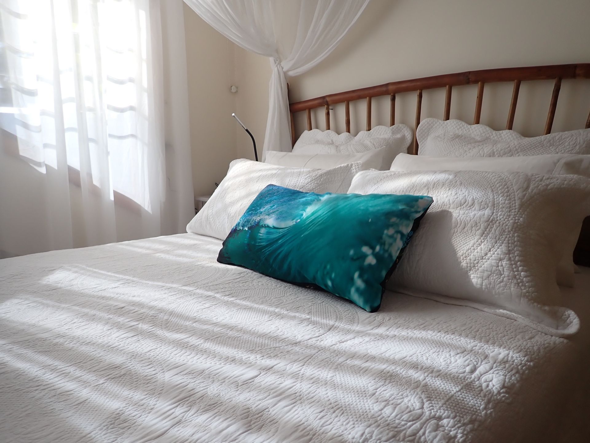 Bright bedroom with a white bed, sheer curtains, and a teal decorative pillow on top