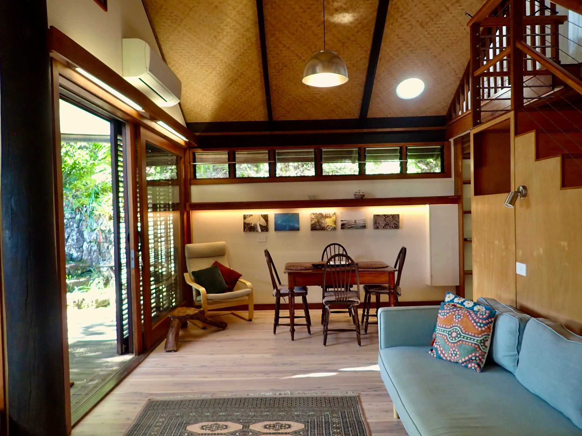 Bright open-plan living room with blue sofa, dining table, and sliding glass doors to greenery.