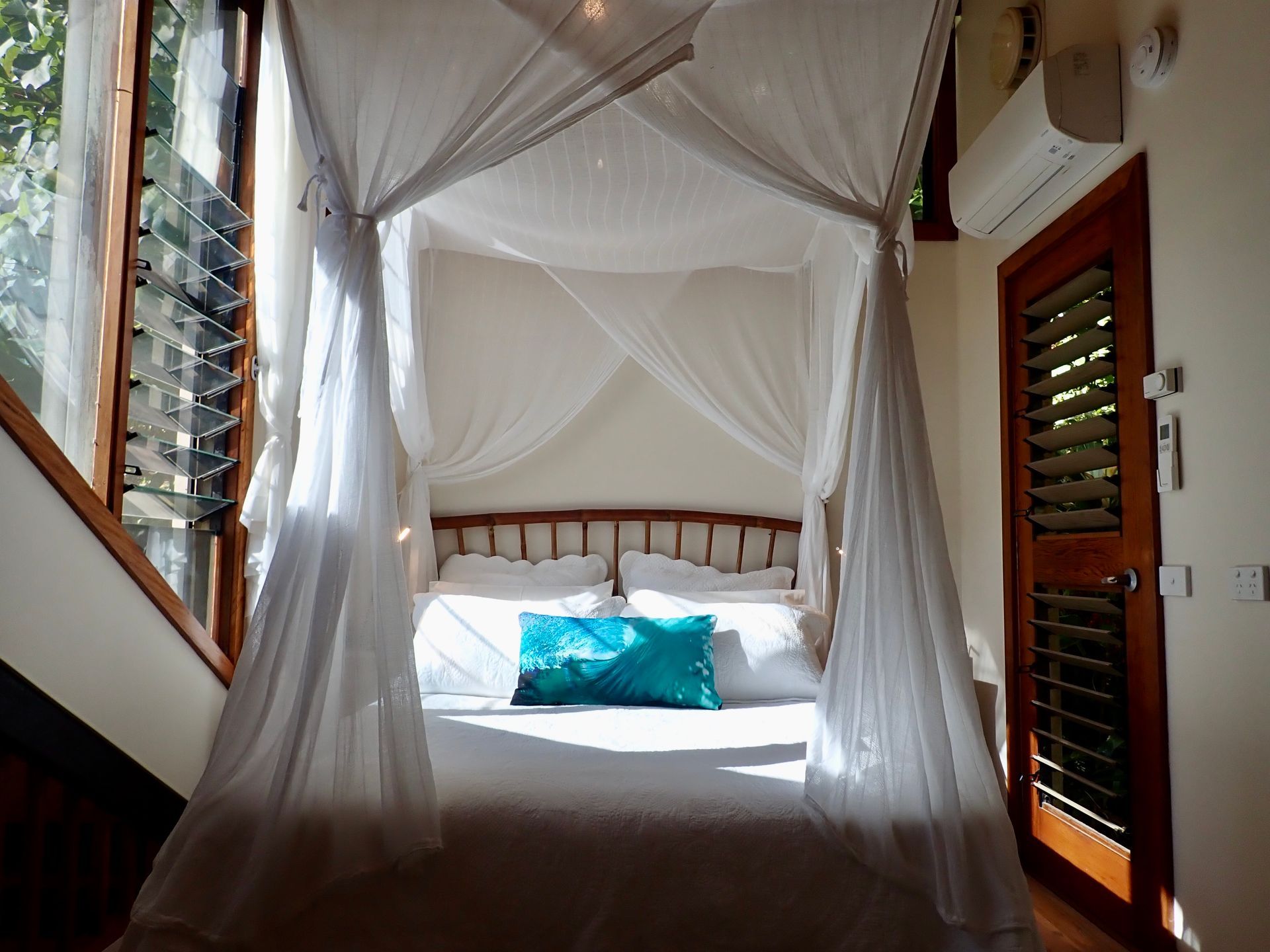 White canopy bed with sheer drapes and turquoise pillows in a bright tropical bedroom