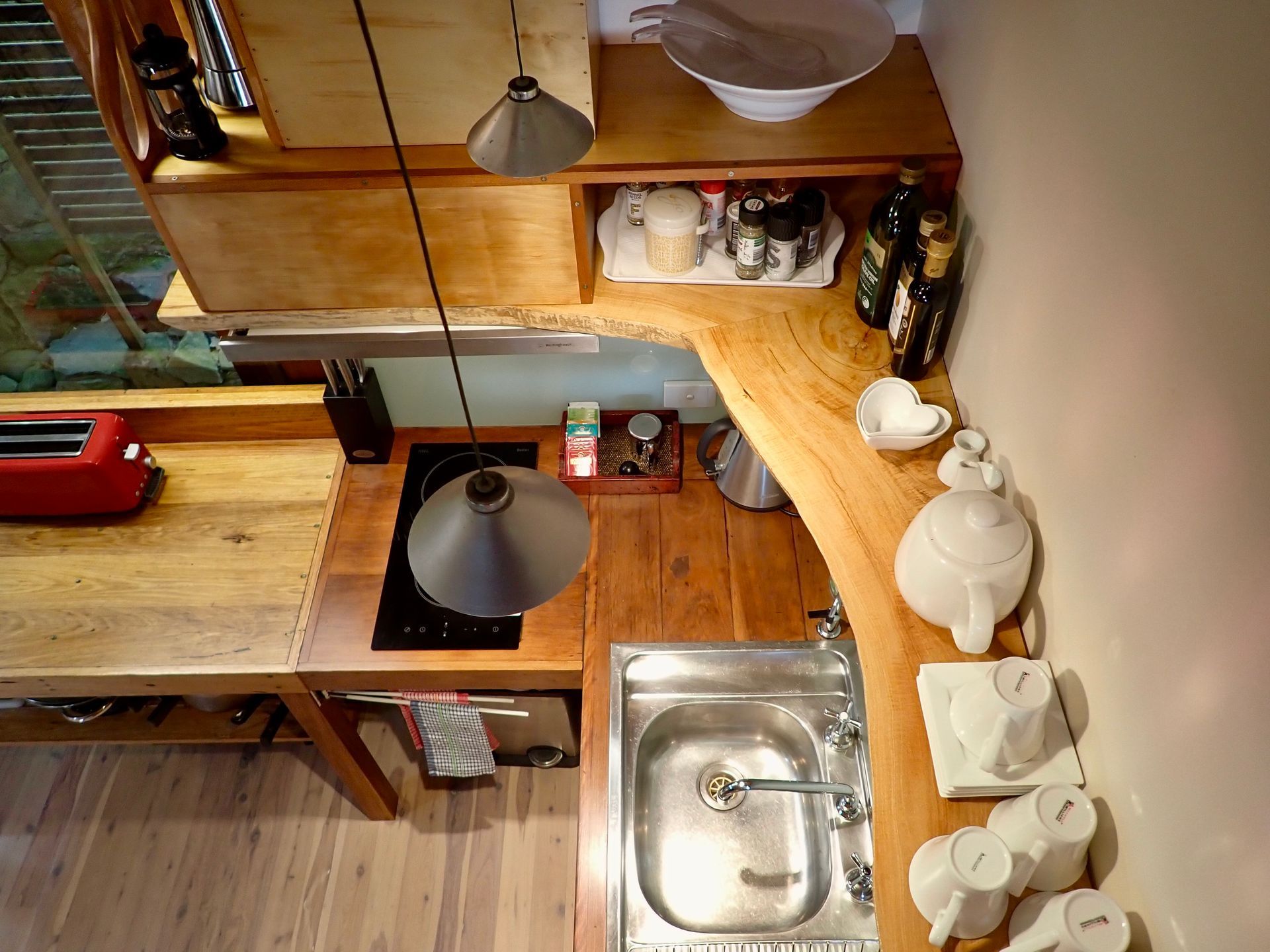 Small kitchen with wooden counters, sink, stove, and white teapot on the right counter.