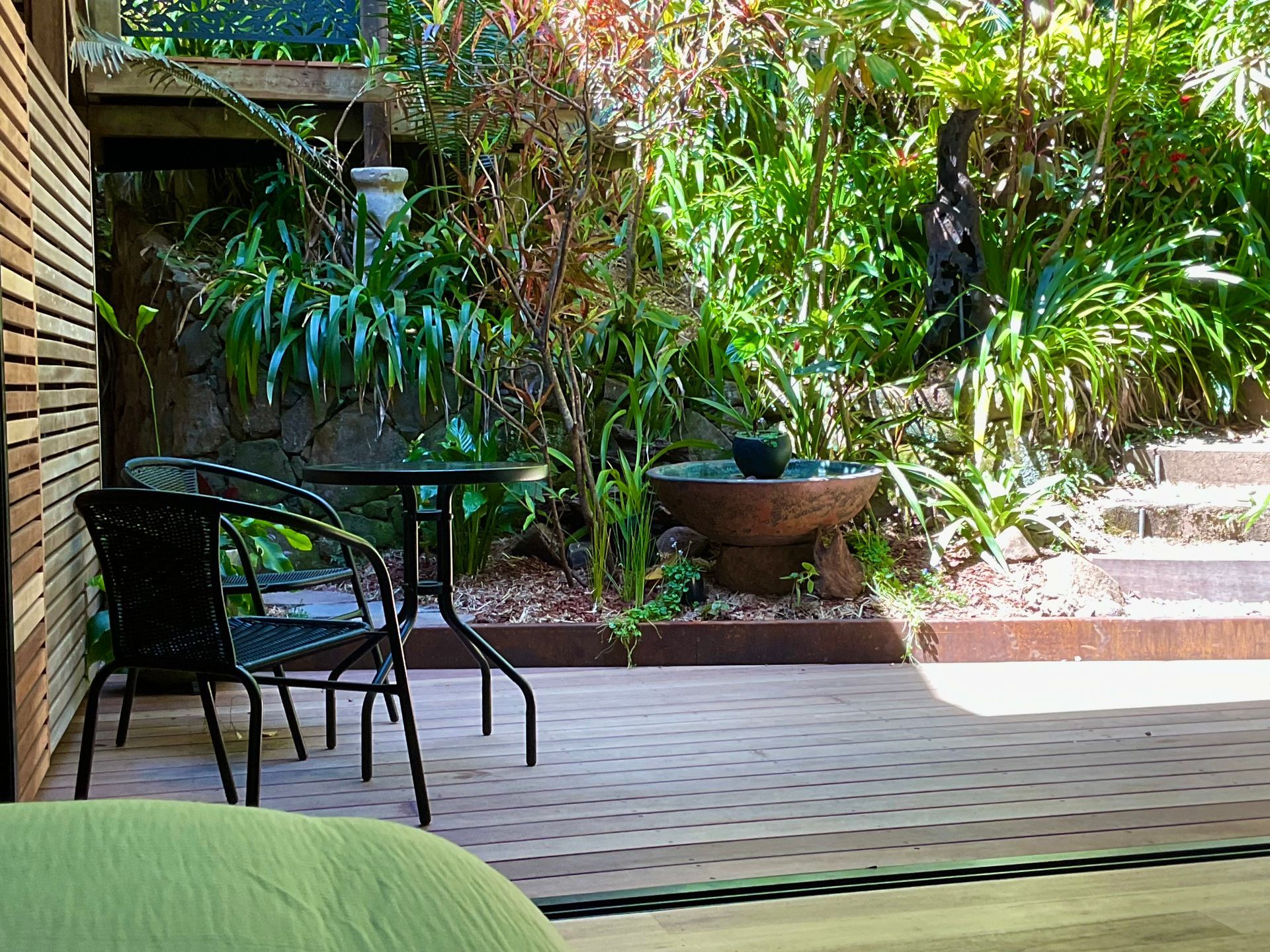 Patio with black metal chairs and table beside lush garden steps and greenery