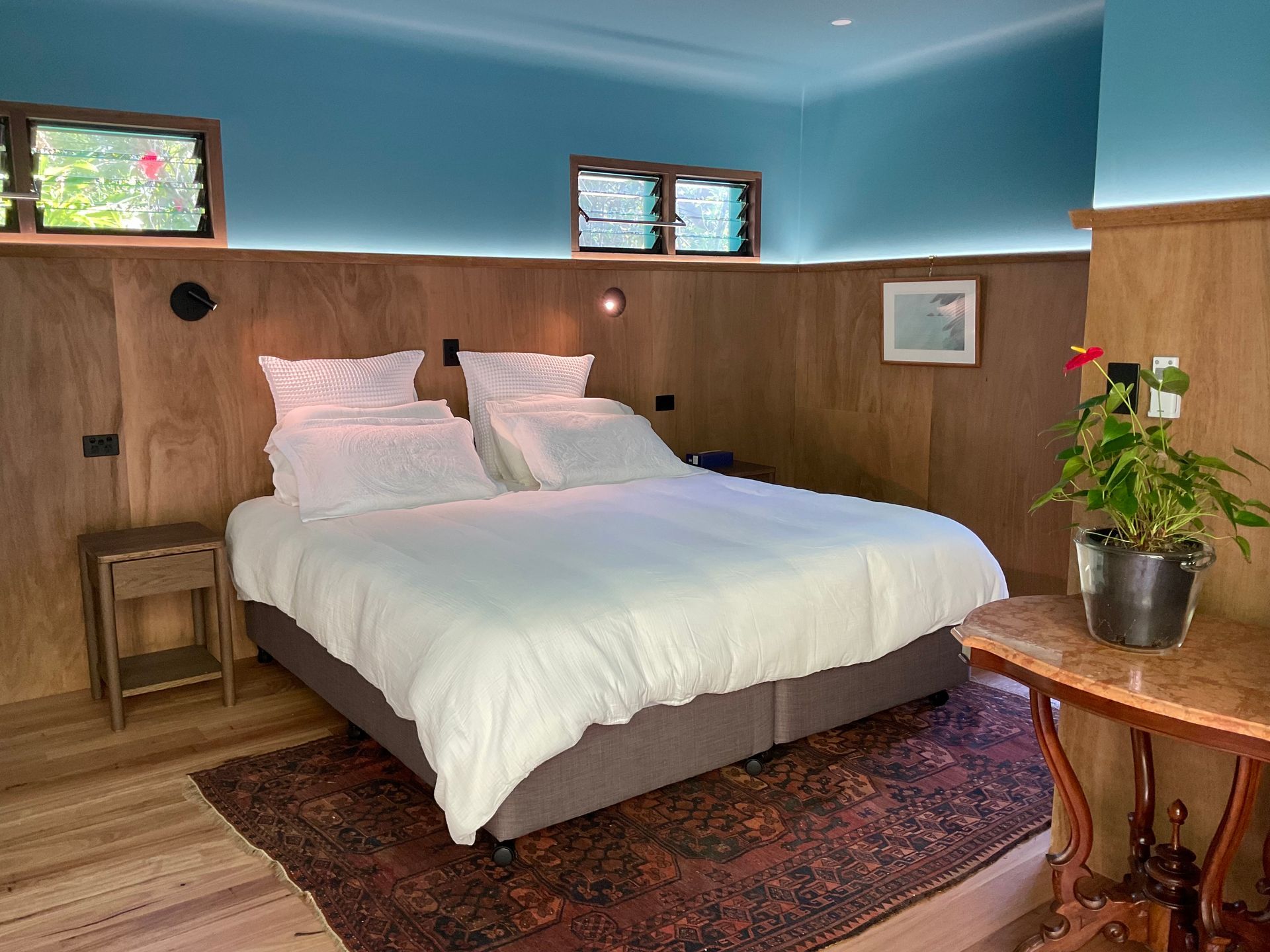 Cozy bedroom with a white bed, wood-paneled walls, blue ceiling, and small windows