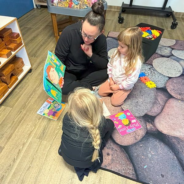 An educator is reading a story book to two children — Mt Ousley Pre School in Fairy Meadow, NSW