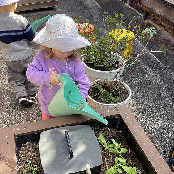 A Little Girl is Watering Plants in a Garden With a Watering Can — Mt Ousley Pre School in Fairy Meadow, NSW