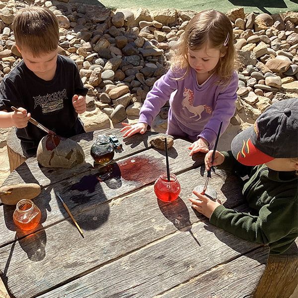 A Group of Children Are Sitting at a Wooden Table Playing With Paint — Mt Ousley Pre School in Fairy Meadow, NSW