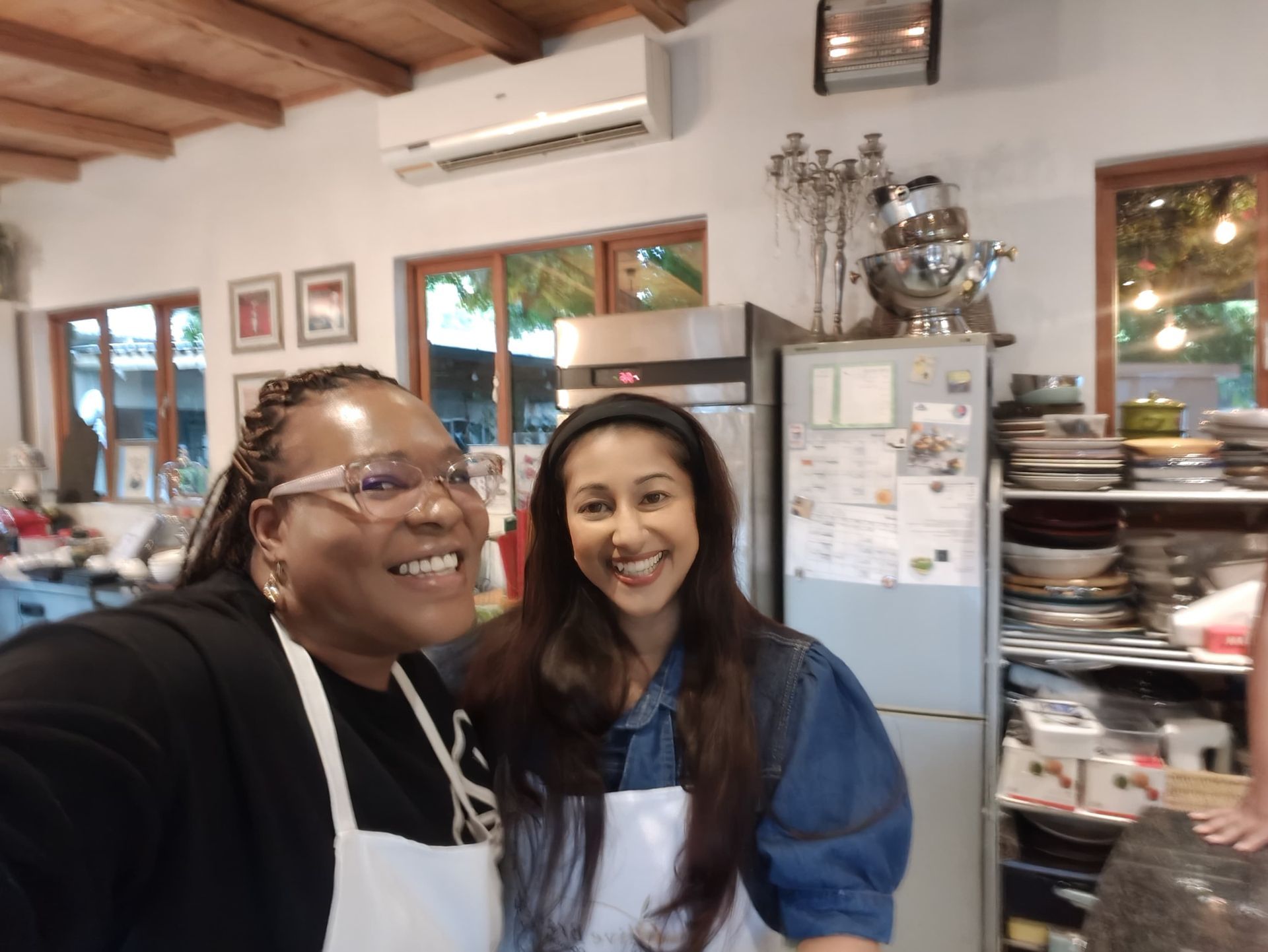 Tricia and Sandy wearing white aprons stand side-by-side in a well-lit kitchen.