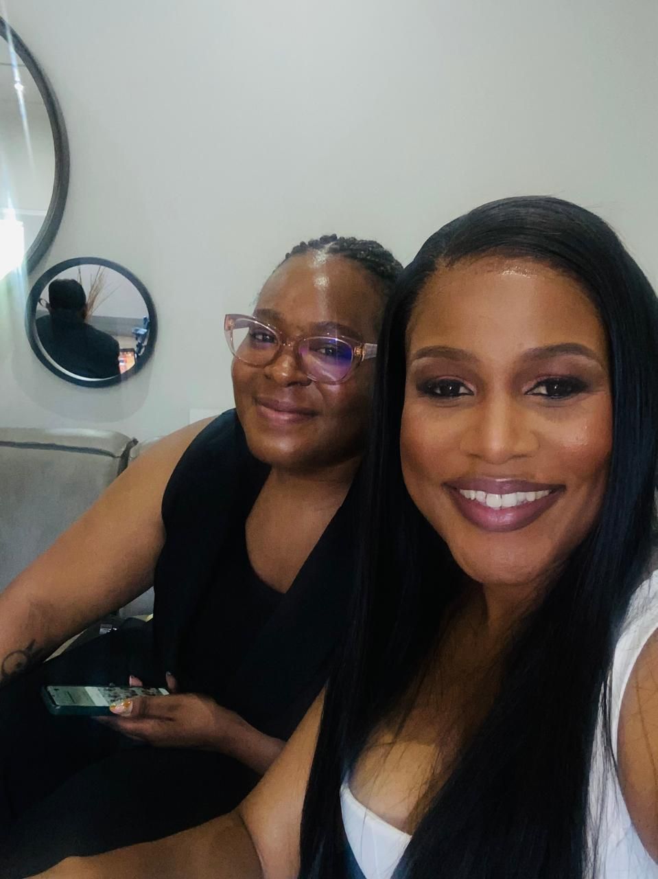Sandy and Zinzisa smiling for a selfie in an indoor setting with round mirrors on the wall in the background.