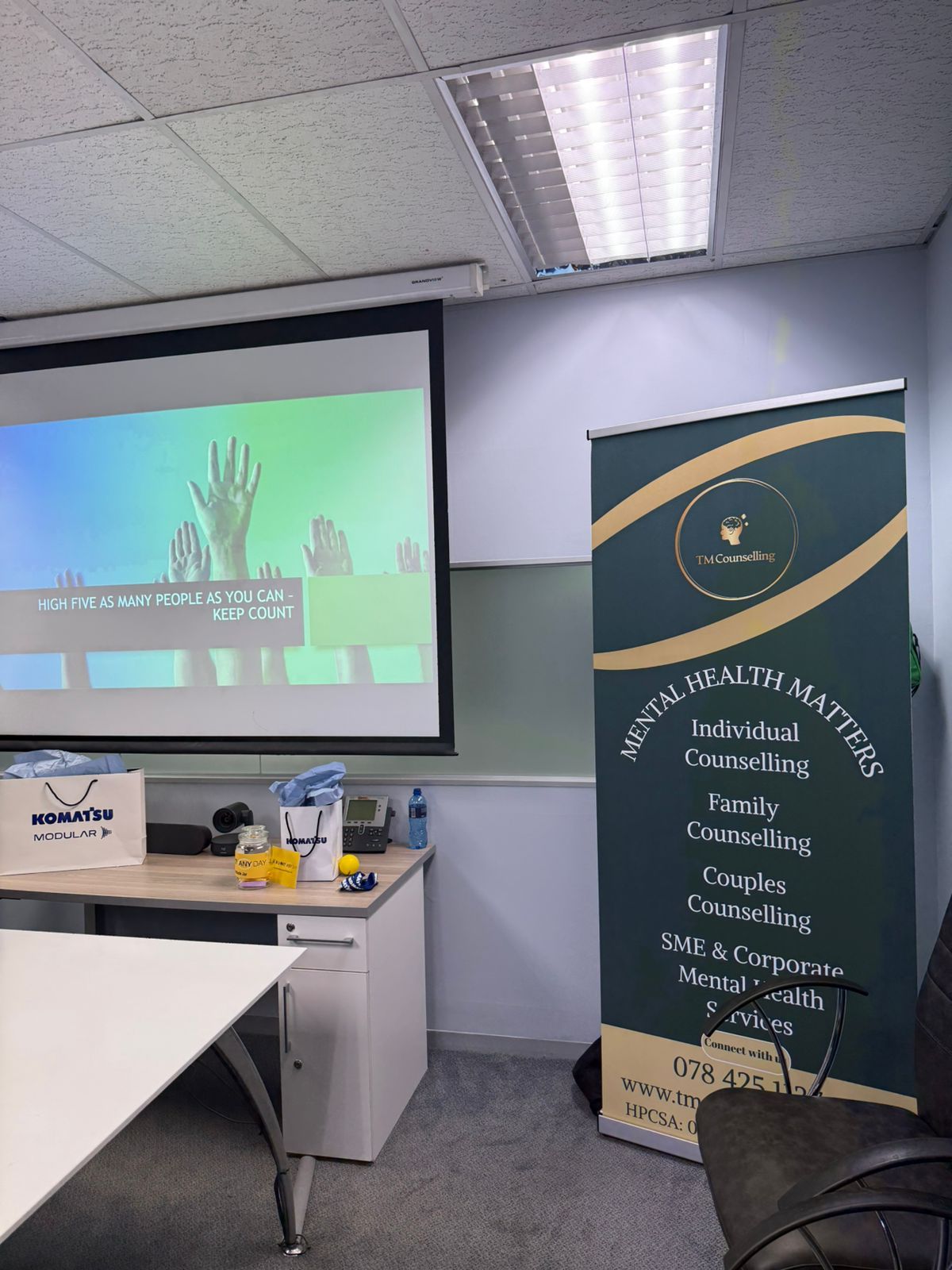 A professional counseling office with a projector screen and a standing TM Counselling banner listing mental health services.