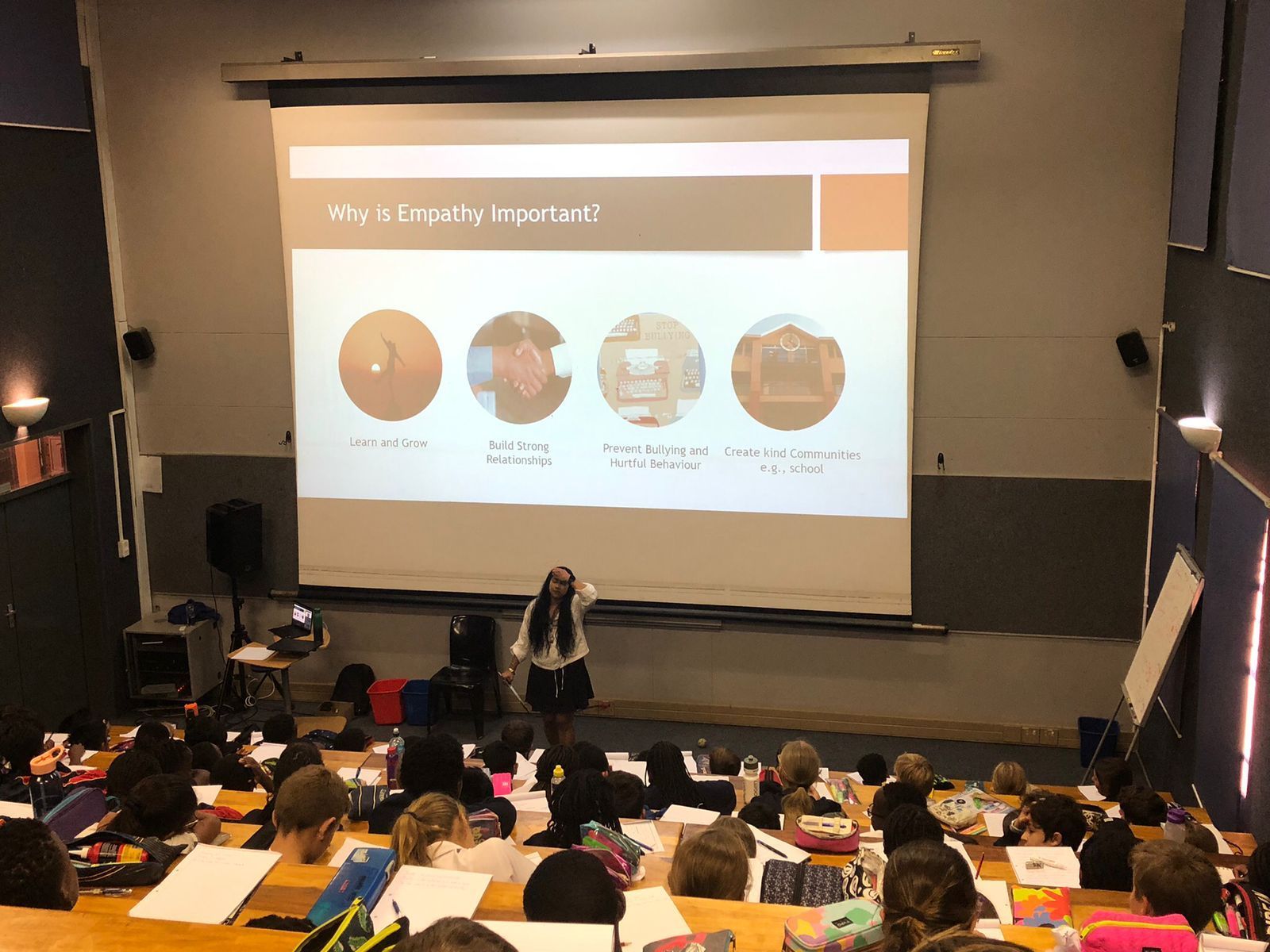 Tricia Moodley stands before a projector screen in an auditorium, presenting on the importance of empathy to an audience.