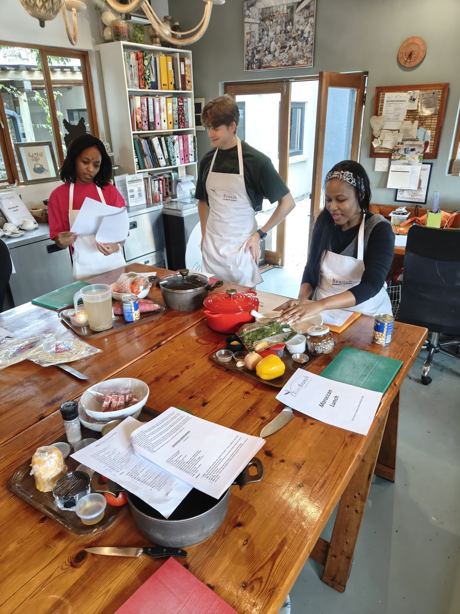 Phozisa, Robert and Zinzisa in aprons stand around a wooden kitchen island preparing a meal.