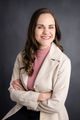 Nadia Liebenberg Registered Counsellor in a beige blazer and pink top, standing with arms crossed against a gray backdrop