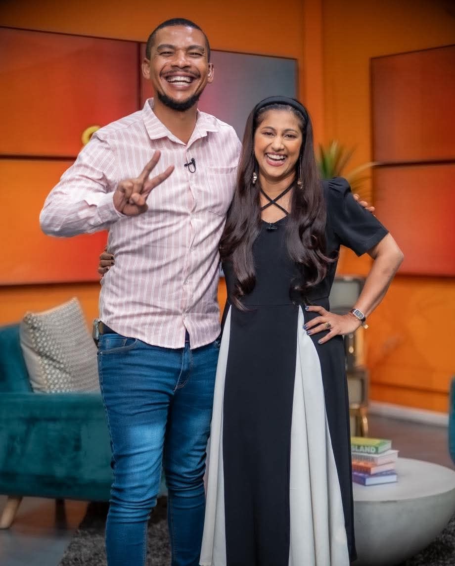 Fran-Rico Lucas making a peace sign and Tricia Moodley smiling in a brightly lit television studio.