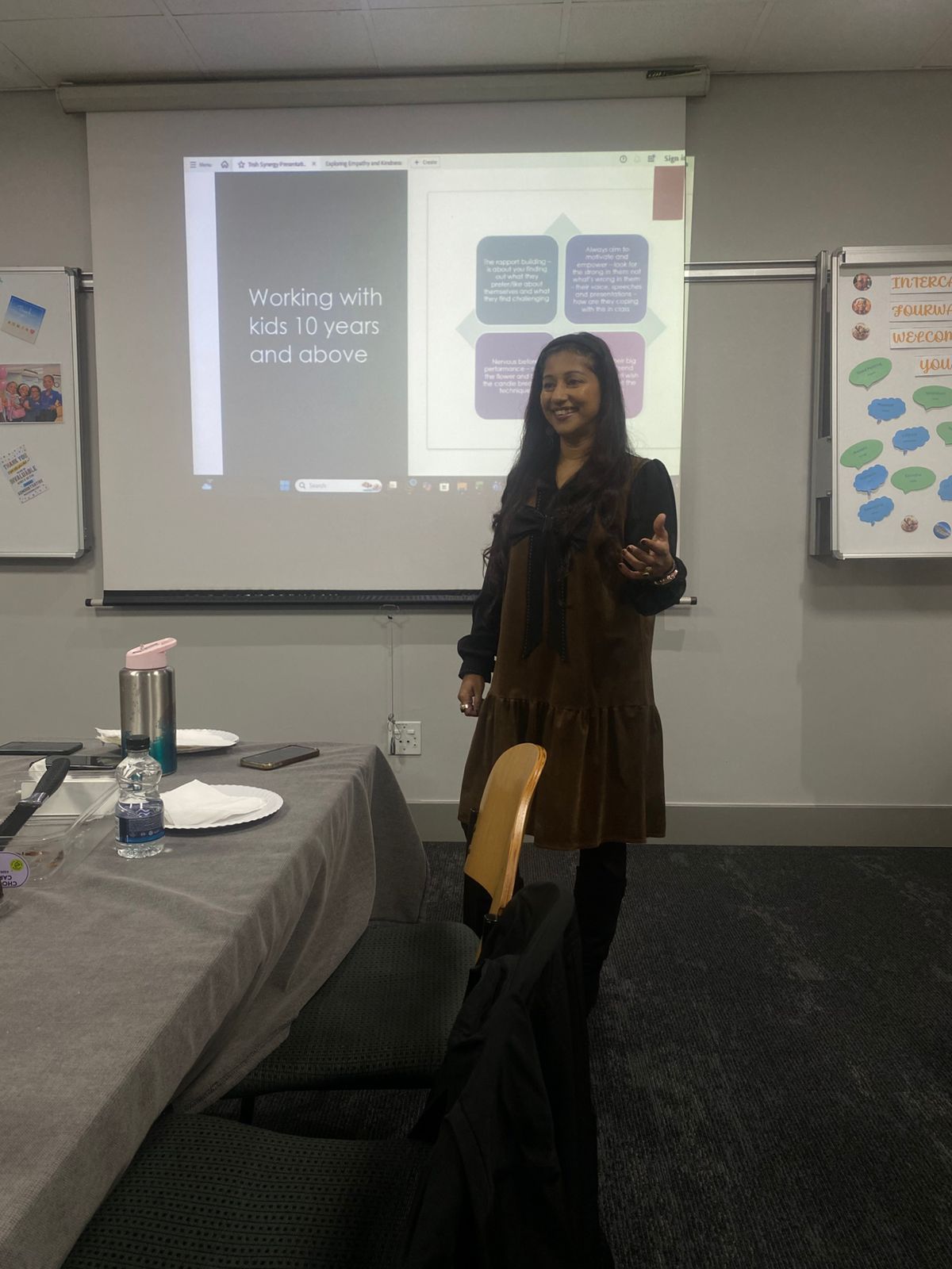 Tricia Moodley speaking beside projected slides in a board room, with tables and chairs in the foreground.