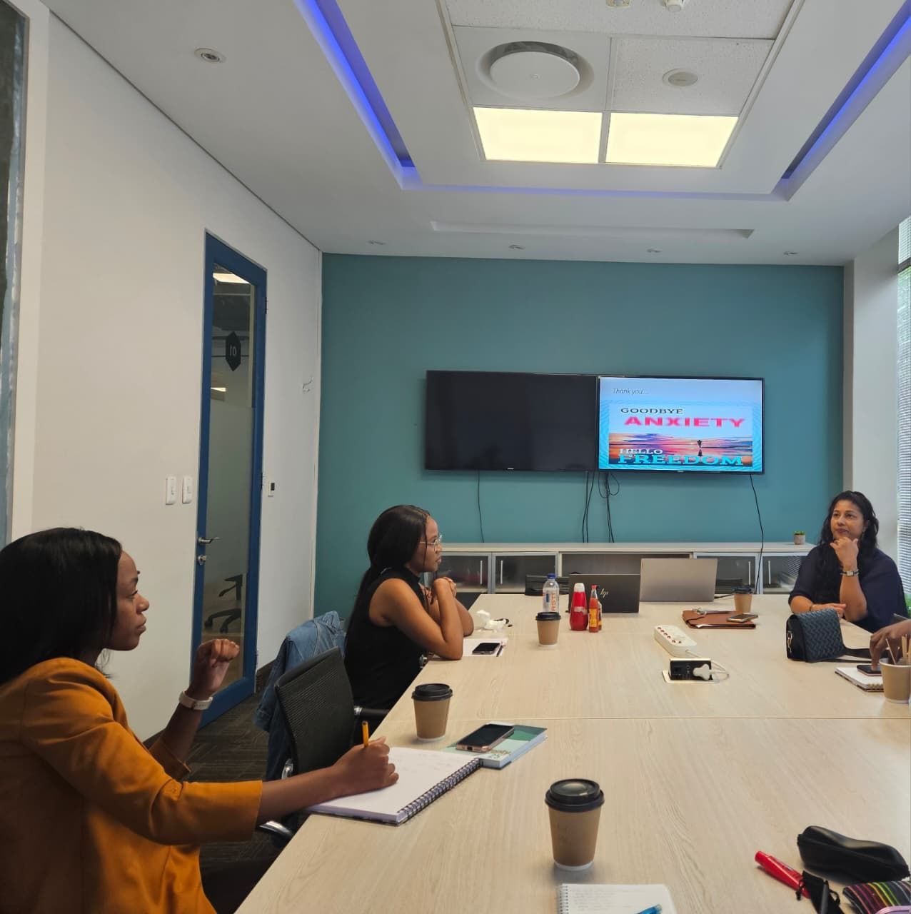 Zinzisa, Phozisa and Tricia  sit at a conference table in an office, attending a presentation on a screen about anxiety.
