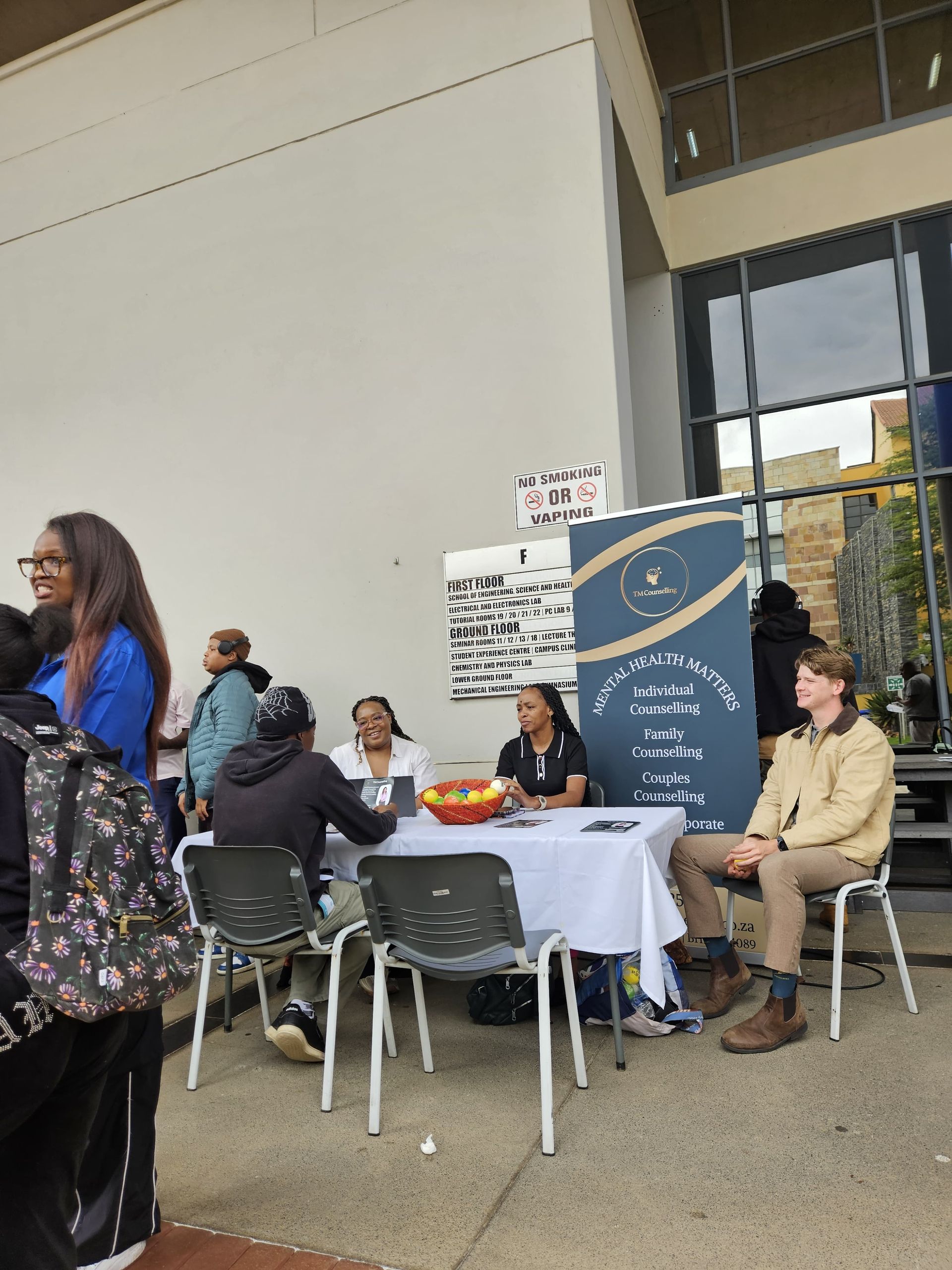 Students sit at a table under a tall TM Counselling promotional banner for a university event.
