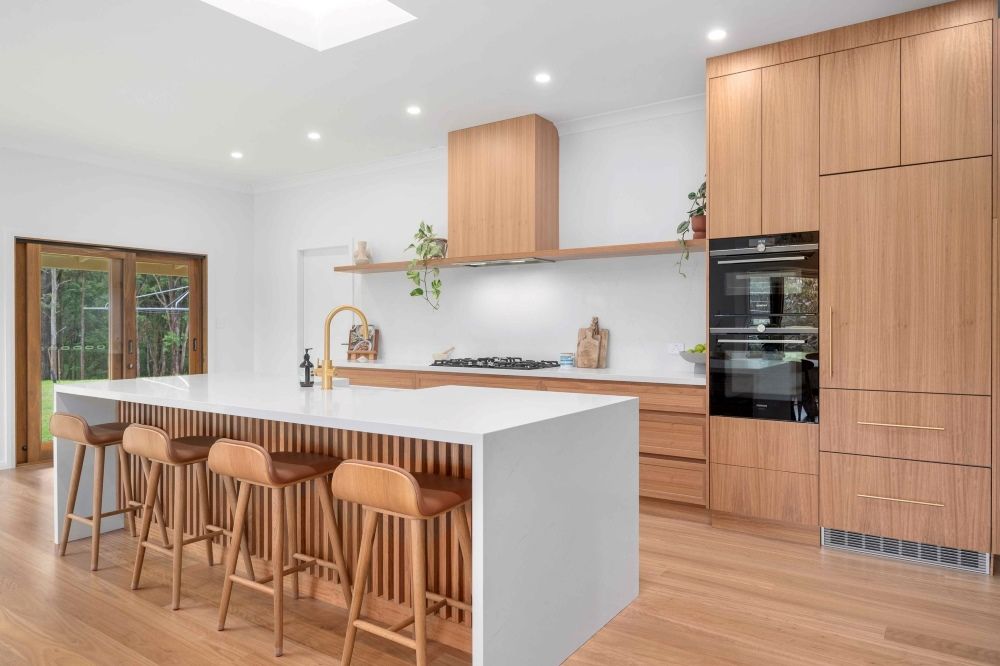 A Kitchen With Wooden Cabinets And Stools And A Large Island — Plumbe Joinery in Woolgoolga, NSW