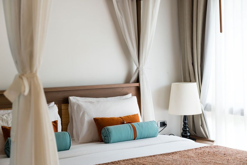 Cozy bedroom with canopy curtains, white bedding, teal pillows, and a bedside lamp