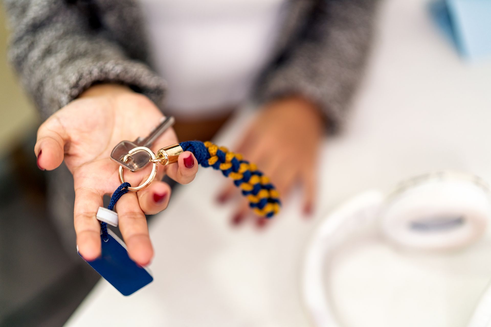 Hand holding a keyring with blue, gold, and orange tags over a white table