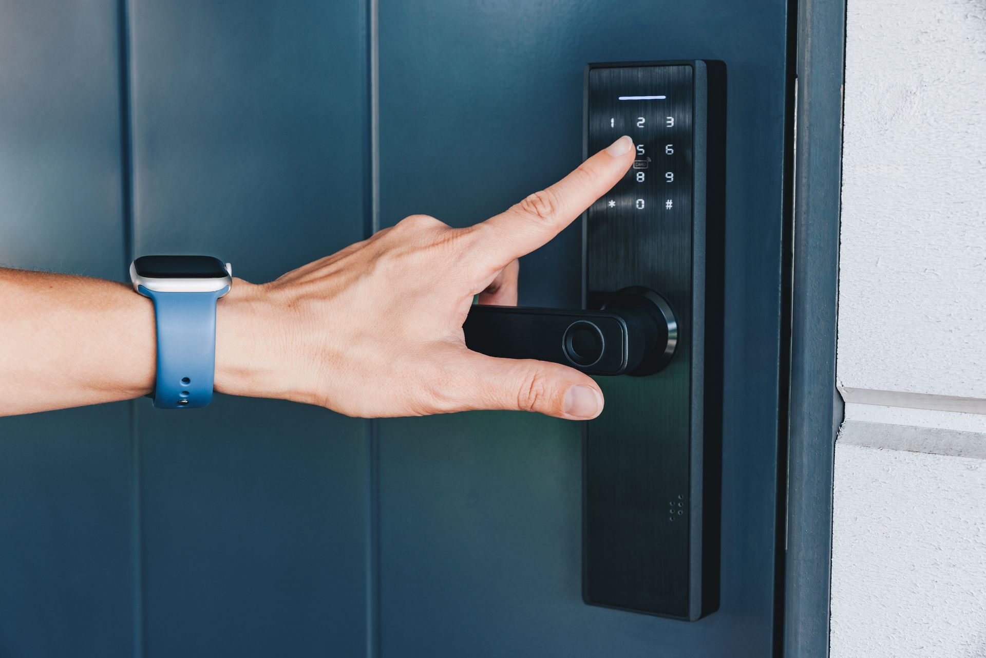 Hand entering a black smart lock code on a dark blue door with a silver handle.