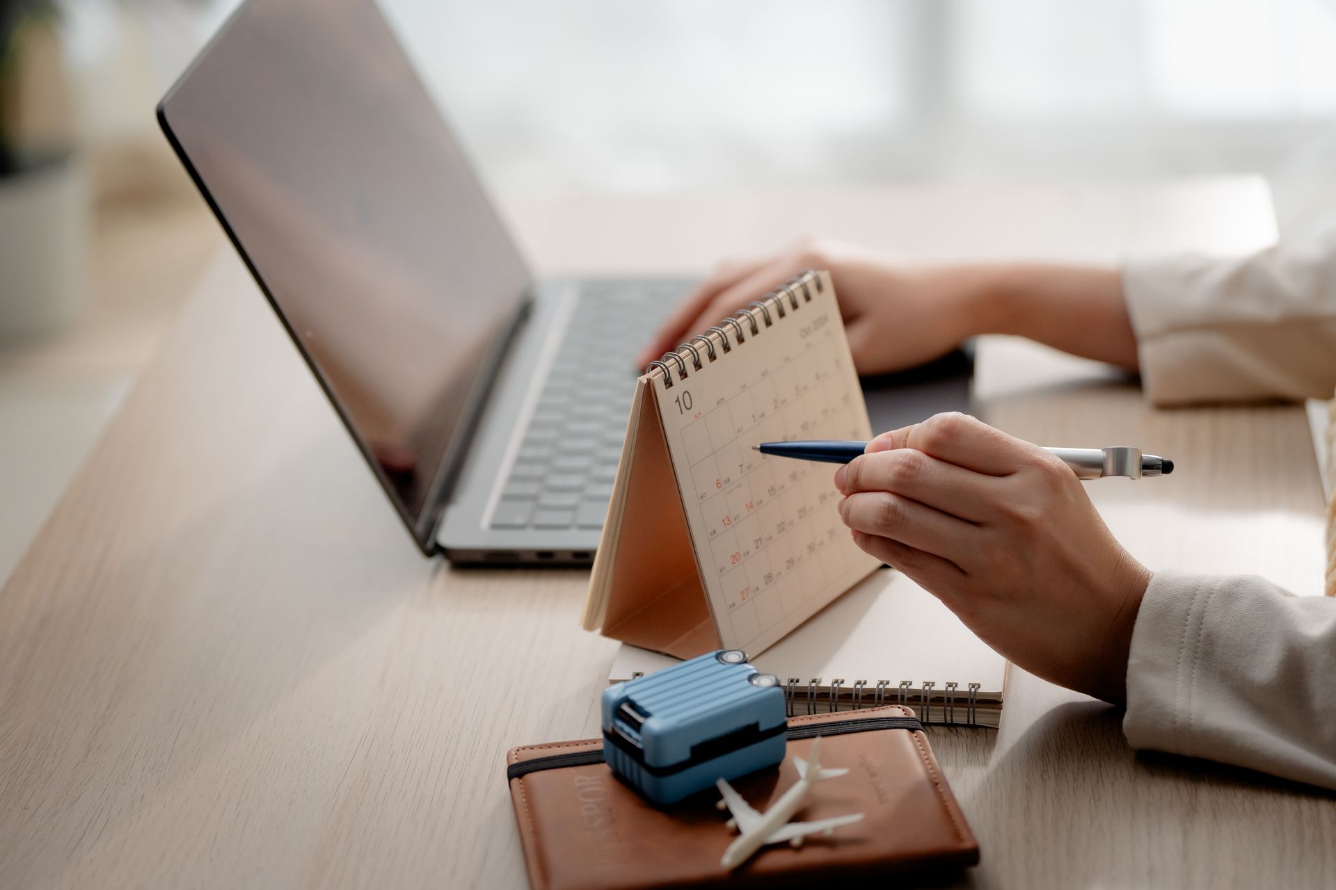 Hands writing in a small desk calendar beside a laptop on a wooden table