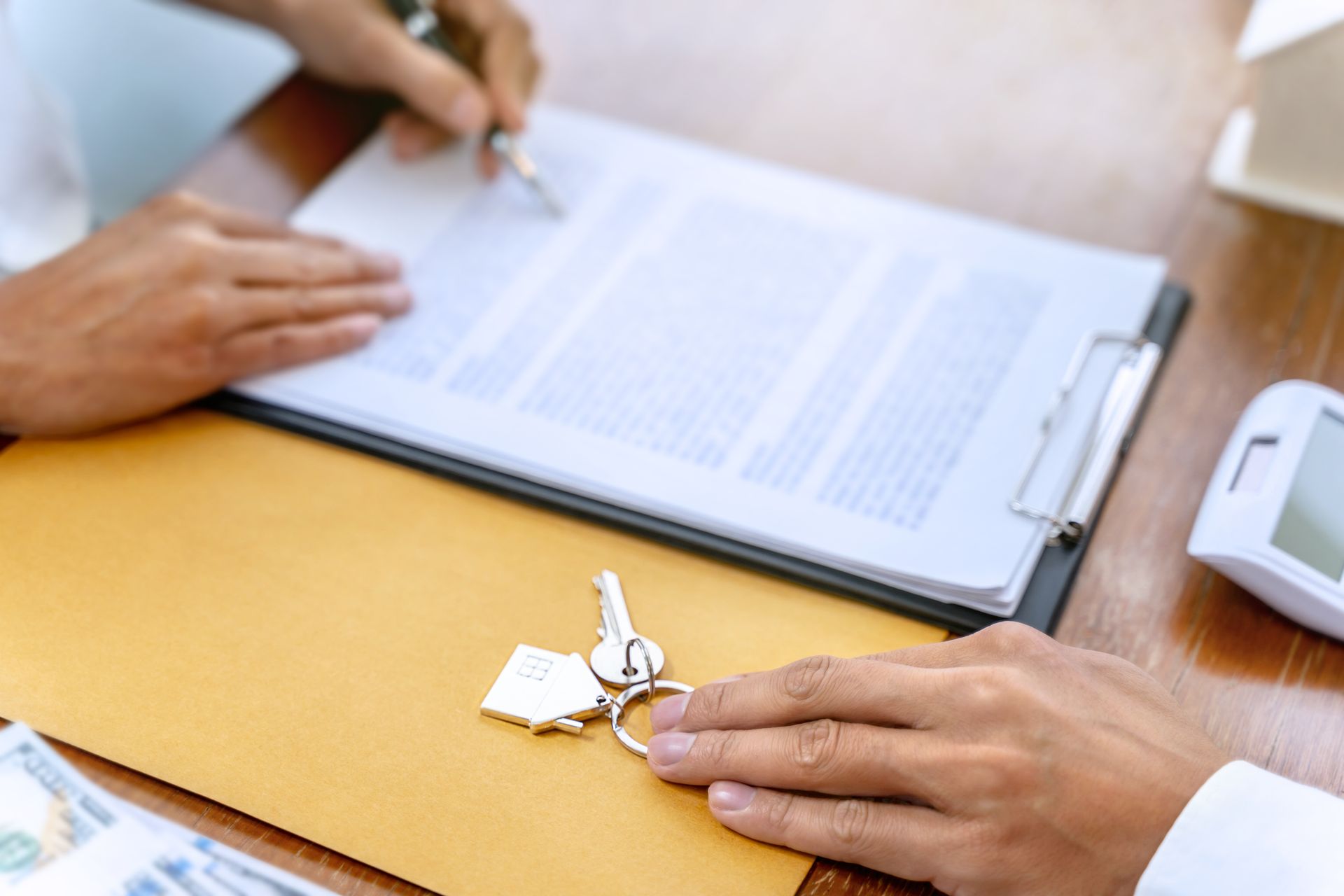 Hands with keys and a pen over a document on a clipboard at a desk