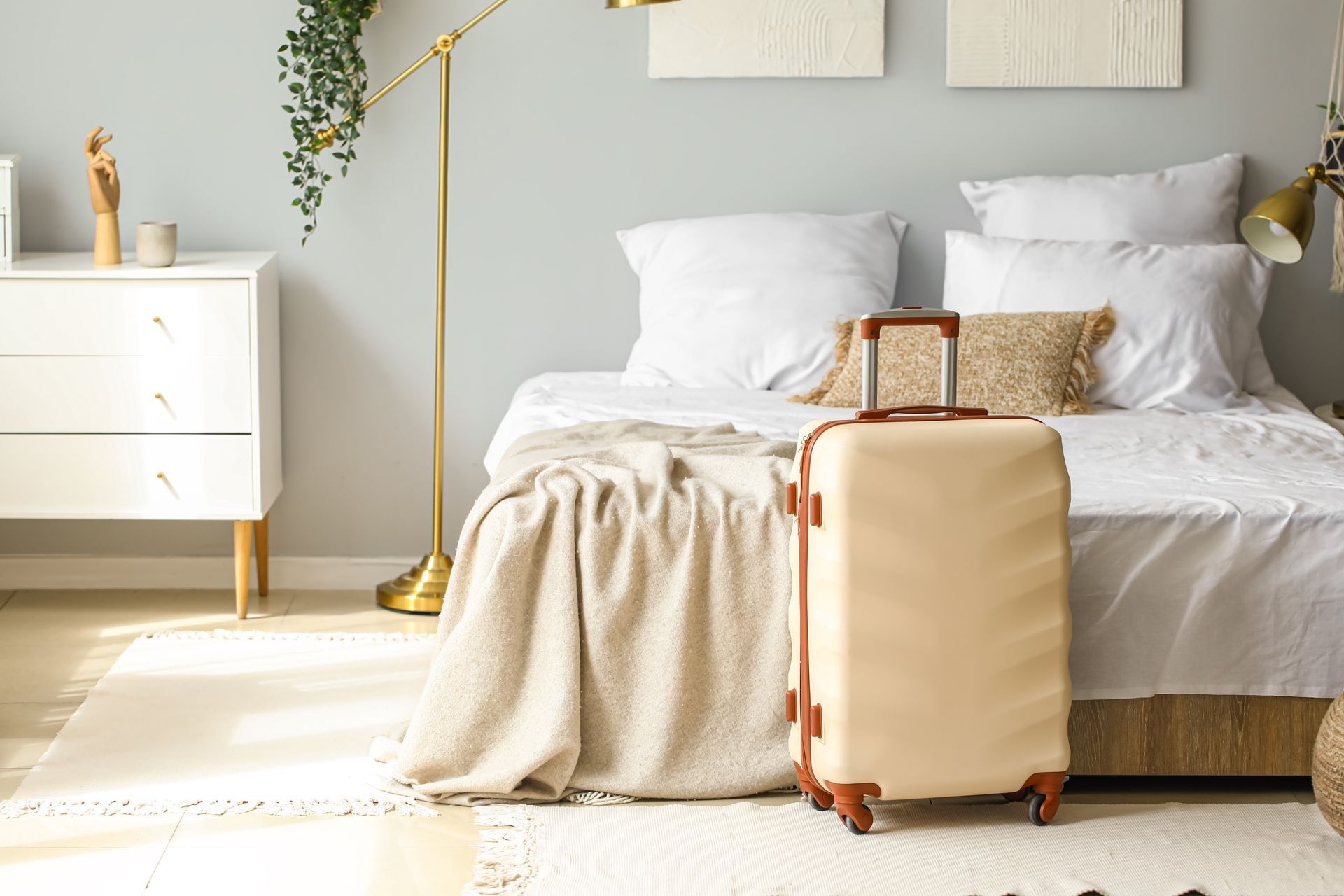 Bright bedroom with white bed, beige throw, and tan suitcase on the floor