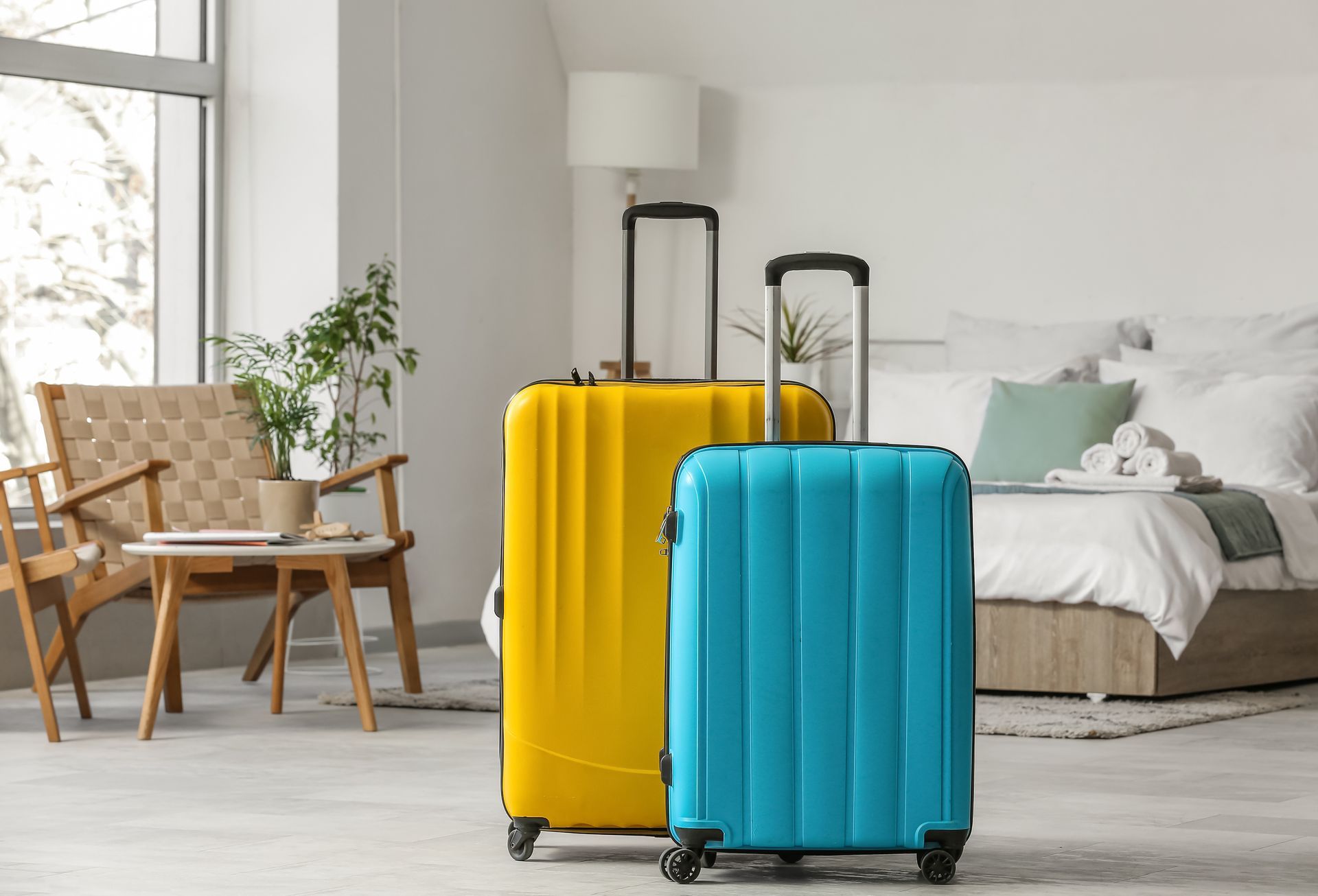 Two colorful suitcases, yellow and blue, in a bright bedroom near a bed and chair