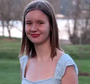 Smiling person in a light blue dress standing outdoors in a park by the water
