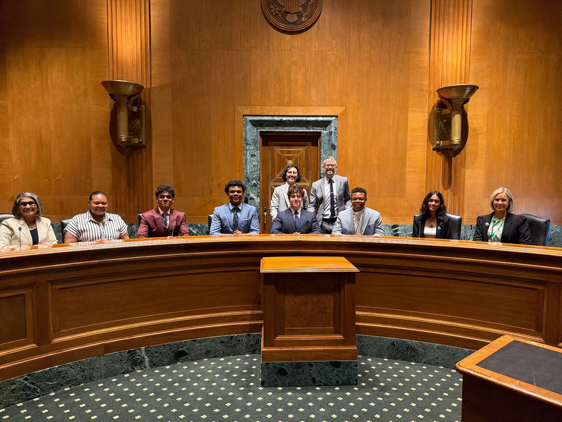 Council members seated behind a curved wooden dais in a wood-paneled chamber with a central podium.