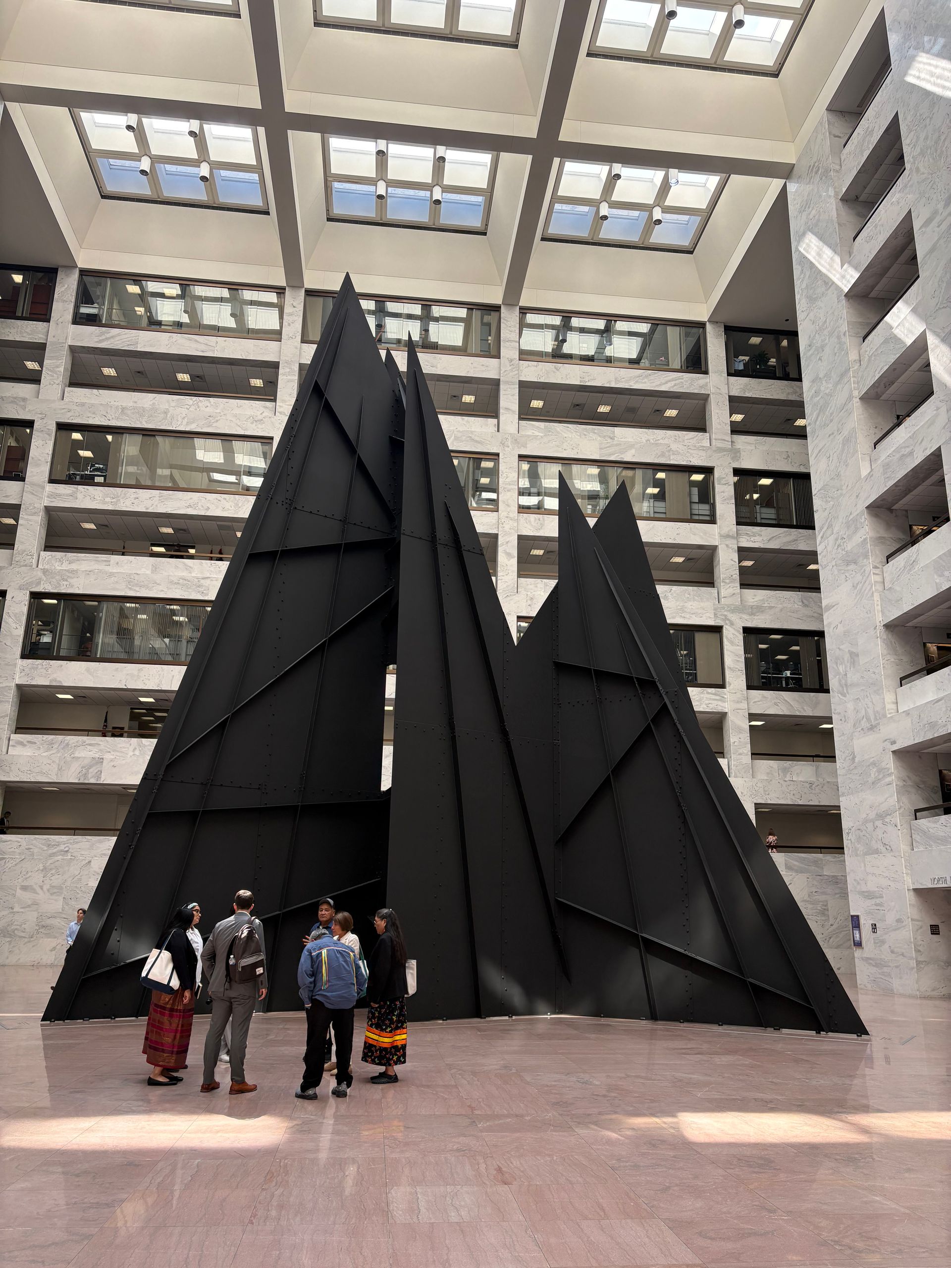 People standing before tall black triangular sculptures in a bright indoor atrium