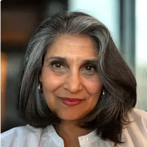Smiling woman with gray hair in a white blouse, seated indoors against a softly blurred background