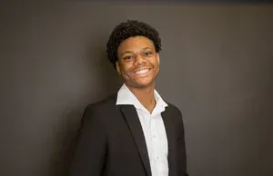 Smiling person in a black blazer and white shirt against a dark background