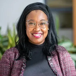 Smiling woman wearing glasses and a maroon jacket against a soft indoor background