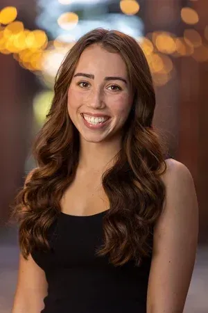 Smiling woman with long brown hair in a black top against blurred warm lights