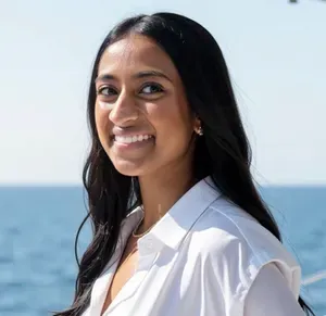 Smiling woman in a yellow top and beaded necklace against a blurred outdoor background