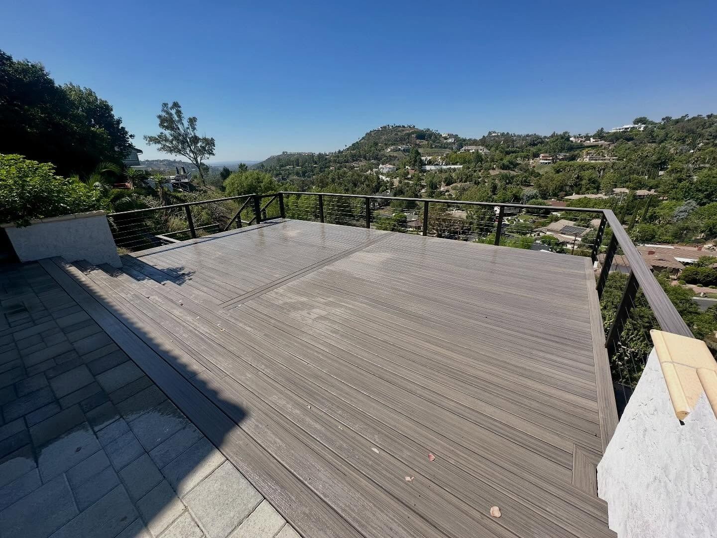 Rooftop deck with gray composite flooring overlooking a green hillside and distant homes