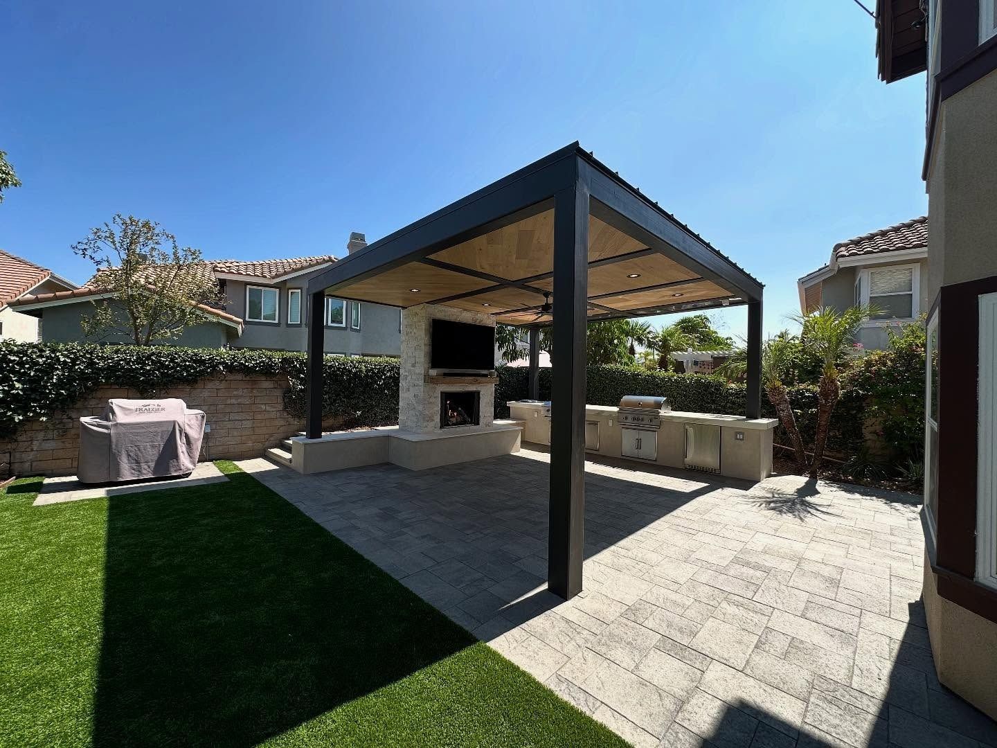 Backyard patio with a covered outdoor kitchen, stone seating, and a paved patio in sunlight