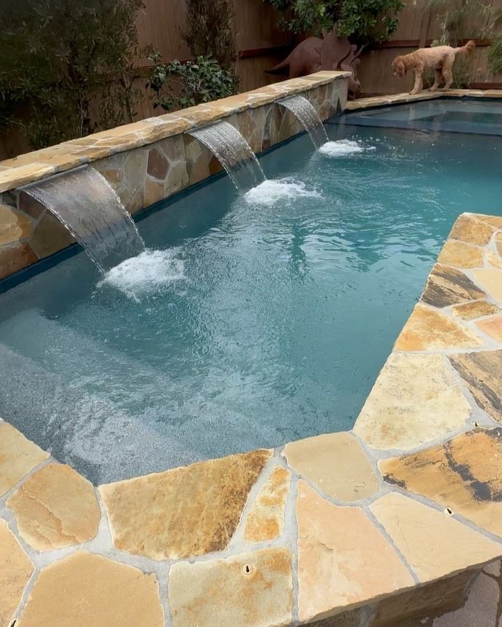 Stone-edged backyard pool with two water cascades flowing into blue water
