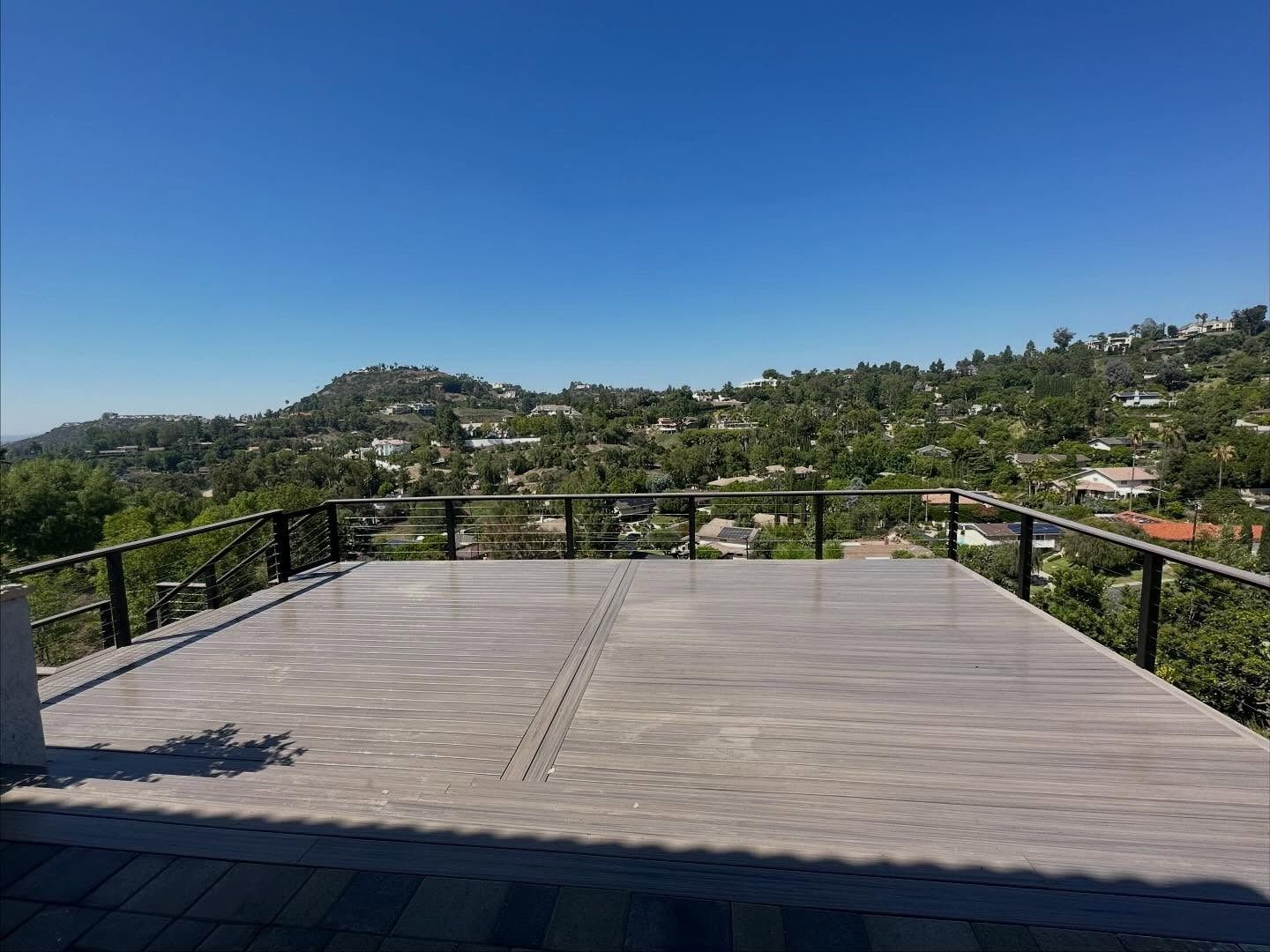 Empty wooden deck overlooking a green hillside under a clear blue sky
