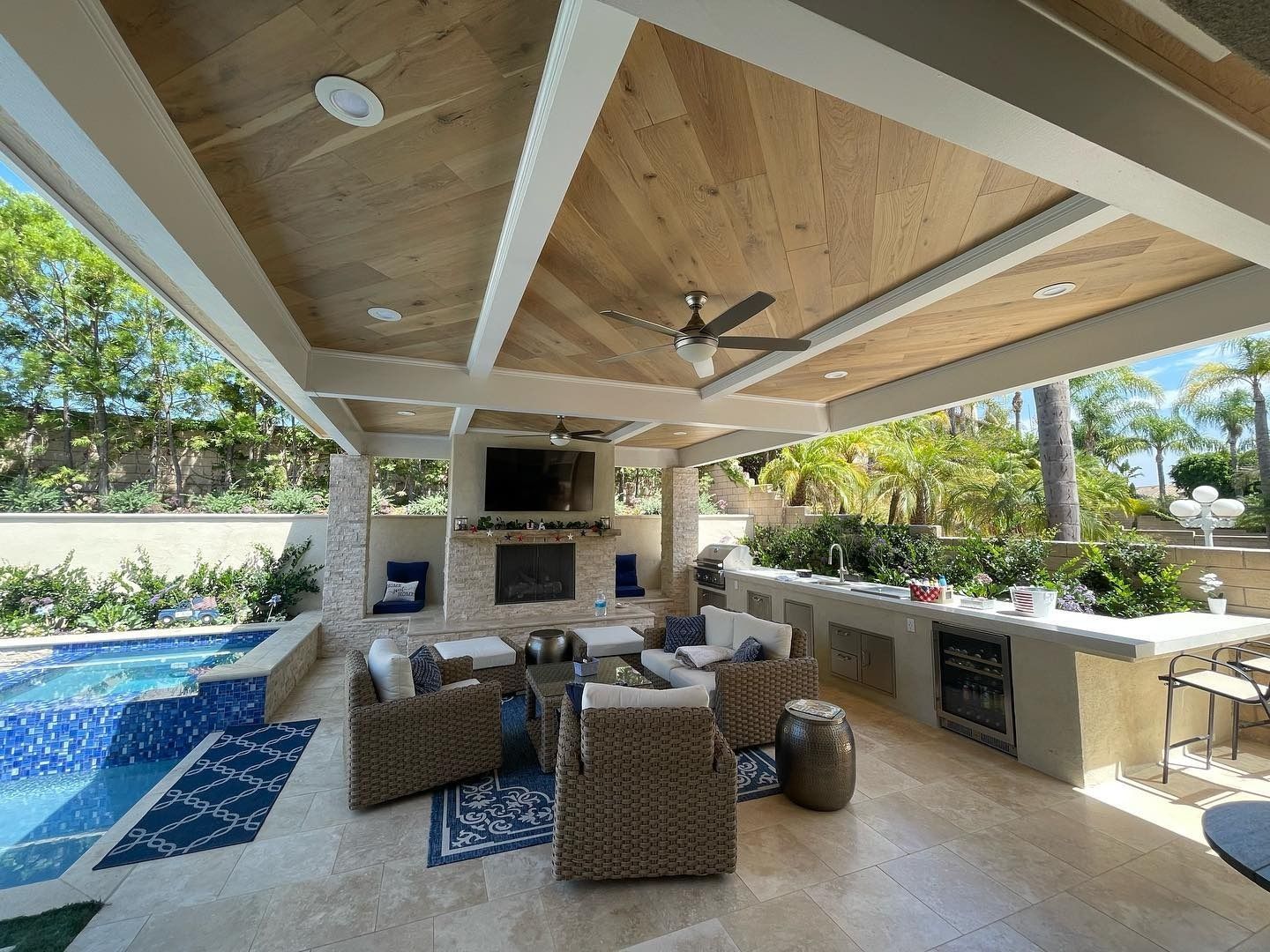 Covered outdoor patio with wicker seating, TV, fireplace, grill, and poolside view