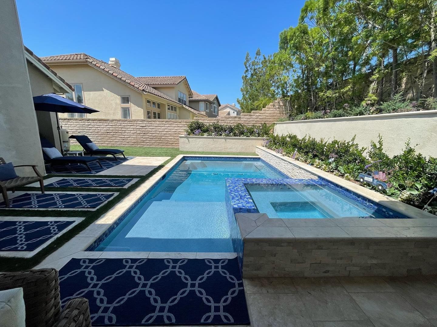 Backyard pool with blue tile, lounge chairs, and a stone patio under a clear sky