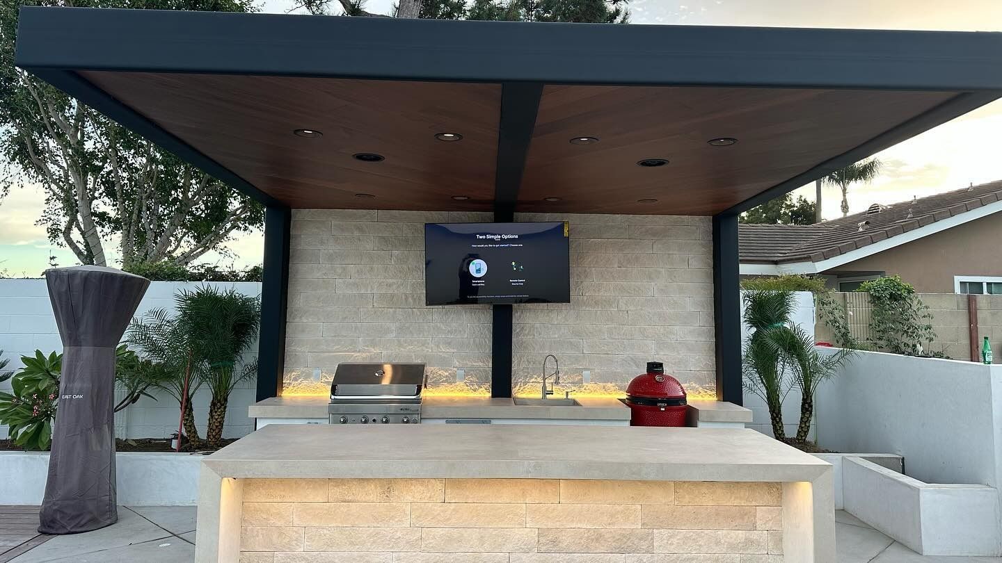 Modern outdoor patio kitchen with stone grill area, large counter, and dark wood canopy