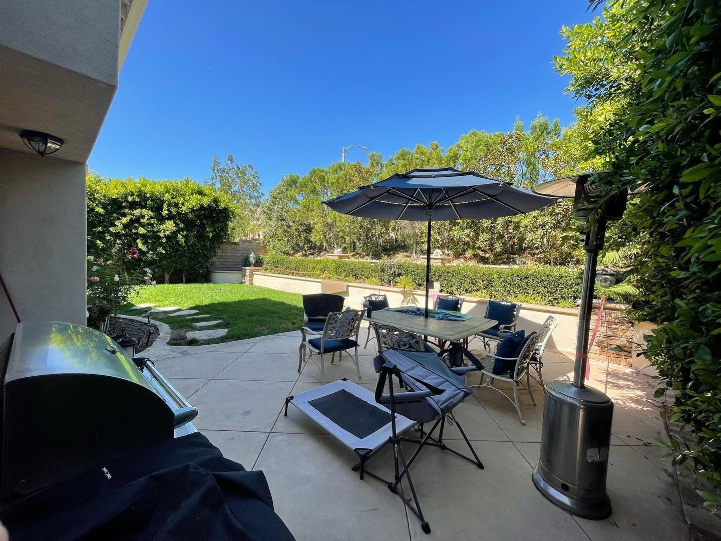 Patio with outdoor dining set, umbrella, lounge chairs, and grill in a sunny backyard