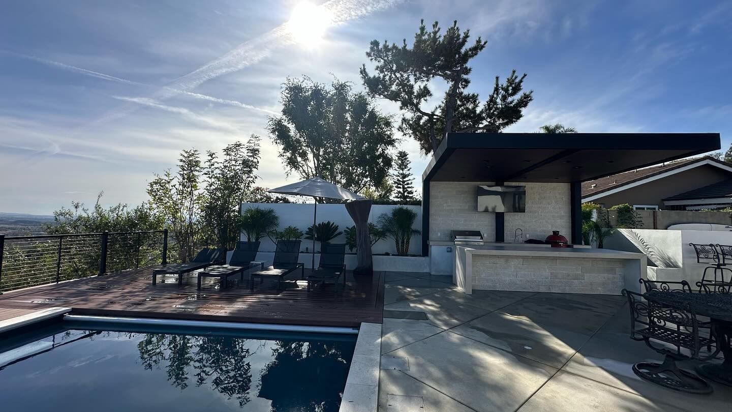 Sunlit backyard patio with a swimming pool, lounge chairs, and a shaded outdoor kitchen area
