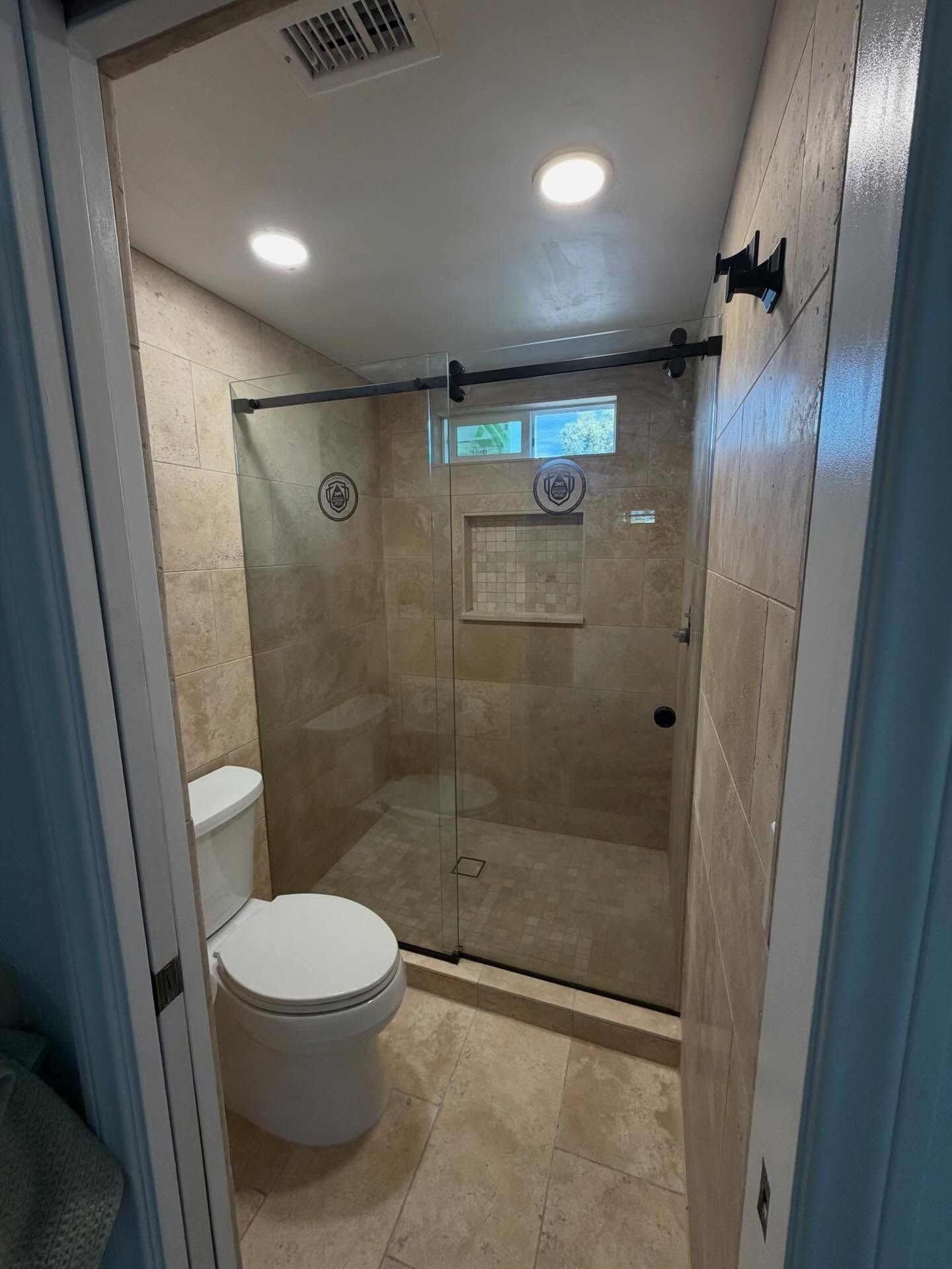 Small bathroom with toilet and glass-enclosed shower, beige tile, and recessed ceiling lights.